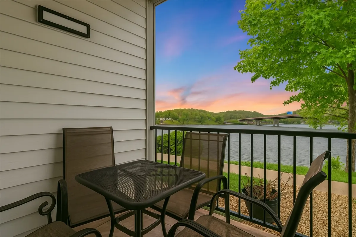 The hero image captures a peaceful balcony with comfortable seating overlooking the tranquil waters of the Lake of the Ozarks. The sun is setting, casting a warm glow over the lake and sky, inviting guests to relax, unwind, and soak in the scenic beauty right from the condo's doorstep.