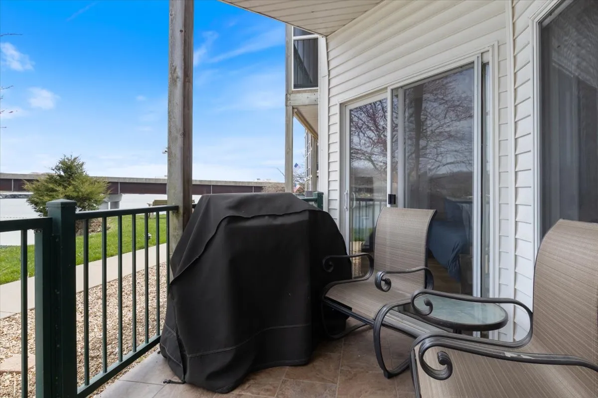 A covered grill, two comfortable outdoor chairs, and a small table make up a welcoming patio scene, suggesting opportunities for barbecues and lakeside drinks. The tranquil outdoor environment invites gatherings and shared meals.