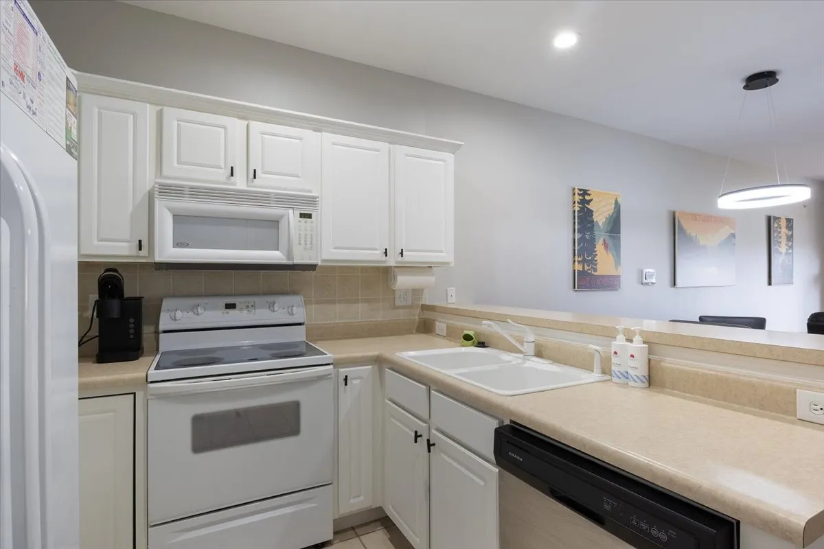 A spacious, modern kitchen featuring white cabinetry, stainless steel appliances, a large kitchen island, and eye-catching artwork on the wall. There is plenty of workspace for meal prep and ample room for multiple cooks or guests to mingle. The open layout connects seamlessly to what appears to be a dining or living area, reinforcing an inviting and social environment.