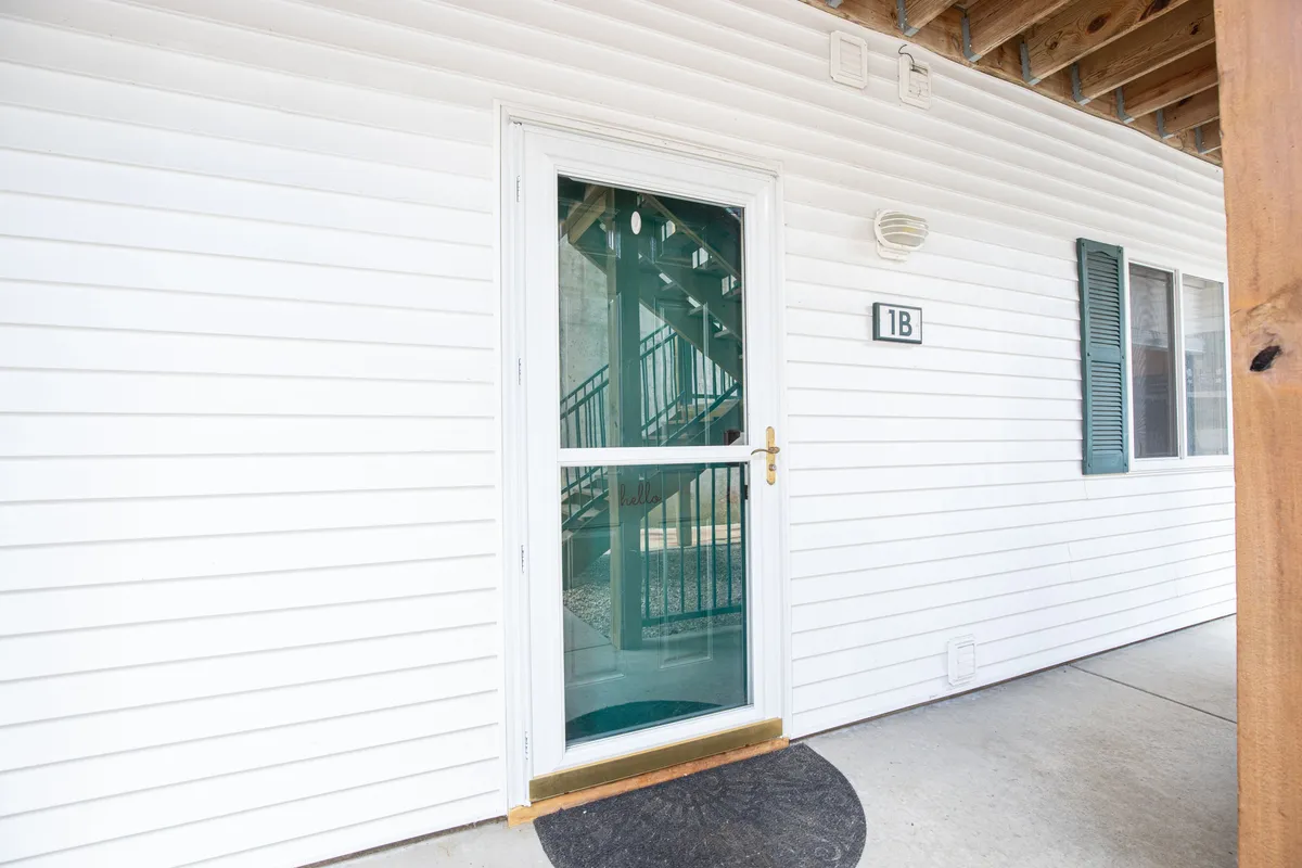 The front entrance of the condo, featuring steps leading up to the door and the house number 1B, creates a warm, welcoming arrival scene. The entryway hints at both the sense of place and ease of access to local attractions.