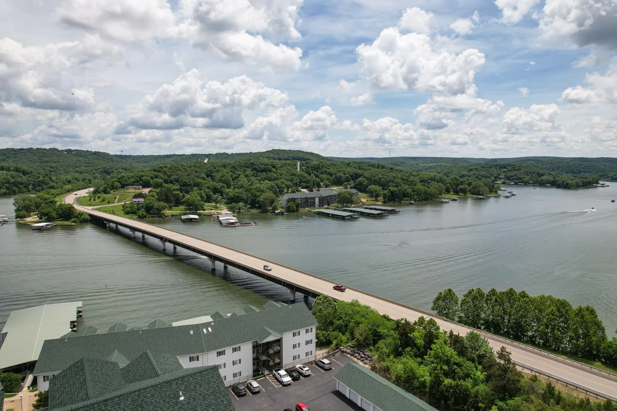 A scenic view featuring a bridge, glistening water, green hills, and boats, inviting guests to explore the nearby natural attractions and trails. The composition speaks to the adventure aspect—kayaking, hiking, and discovering the surrounding landscape.