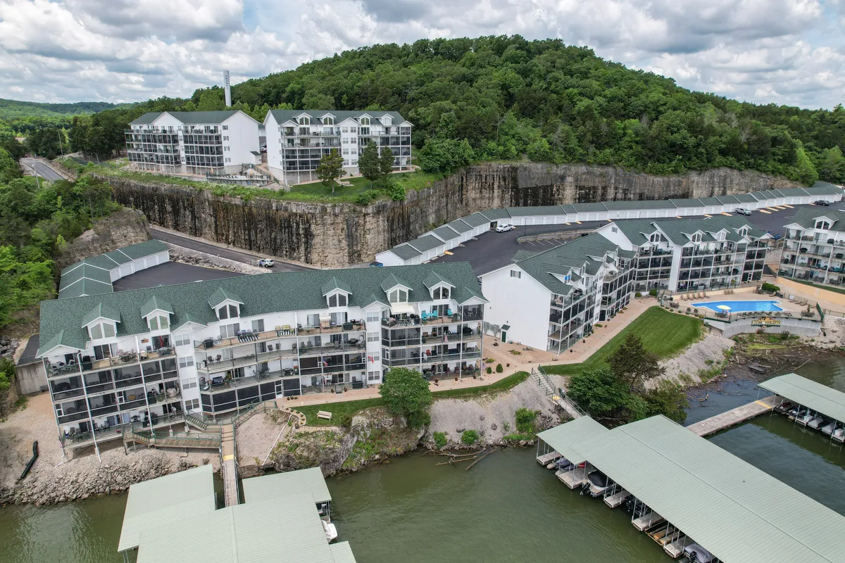This image captures the tranquil waterfront setting of Lake Escape, with multi-story buildings nestled by the water and green hills in the backdrop. The scene emphasizes direct access to the lake, perfect for boating, fishing, or relaxing by the shore, and hints at both the serenity and adventure available just steps away.