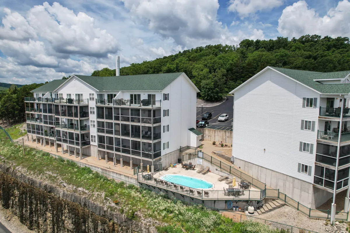This exterior image features the sparkling swimming pool surrounded by lounge chairs and balconies, set against green surroundings. The pool area radiates a relaxed, resort-like atmosphere and suggests opportunities for swimming, sunbathing, and socializing just steps from the condo.
