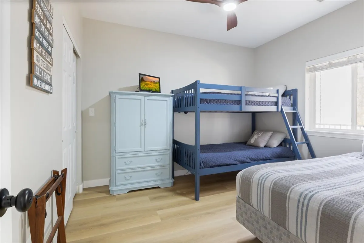 A cheerful secondary bedroom with a bunk bed, blue dresser, and playful bedding. The space feels welcoming and functional, ideal for children or guests. The layout offers comfort and ample storage.