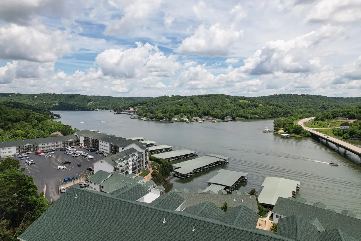 A peaceful, wide-angle view of the lake, dock, green hills, and community buildings, capturing the tranquil lakeside setting. The dock and water invite boating, fishing, and strolls by the water’s edge, tying directly to the section's focus on lakefront access and outdoor adventure.