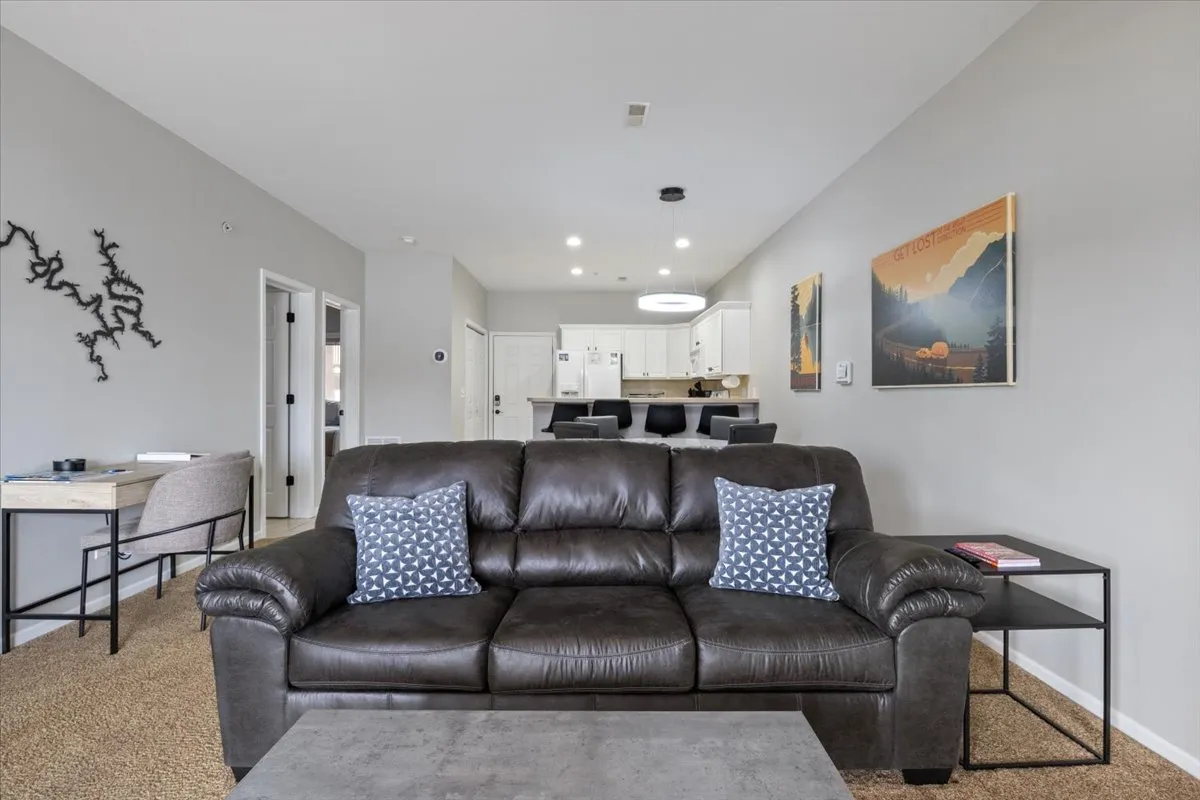 An open-concept living and dining area with a leather couch adorned with blue pillows, a dining table in the background, and the kitchen visible through the open layout. Artwork on the wall and updated floors contribute to a modern, cohesive look ideal for hosting gatherings.