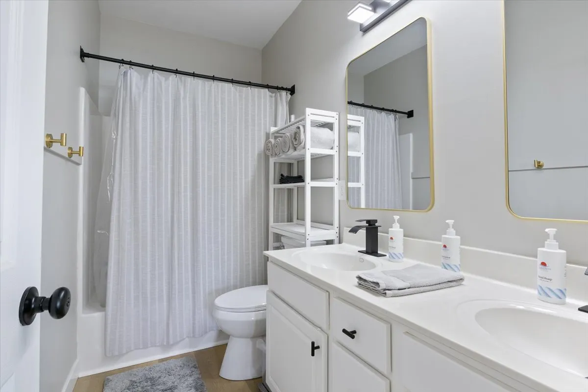 A spacious, modern bathroom with a dual sink vanity, large mirror, and a well-lit shower area. The organized setting and stylish fixtures suggest privacy, comfort, and room for multiple guests.